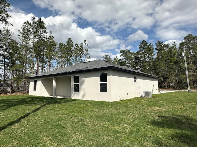 rear view of property featuring a shingled roof, stucco siding, a yard, and central air condition unit