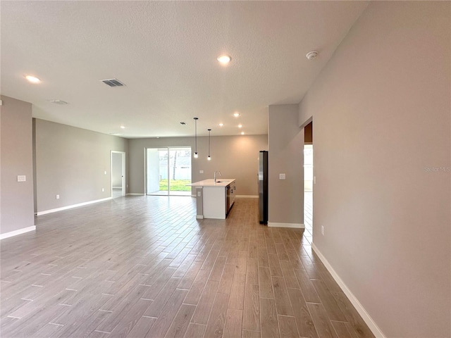 unfurnished living room featuring a textured ceiling, a sink, visible vents, and light wood-style floors