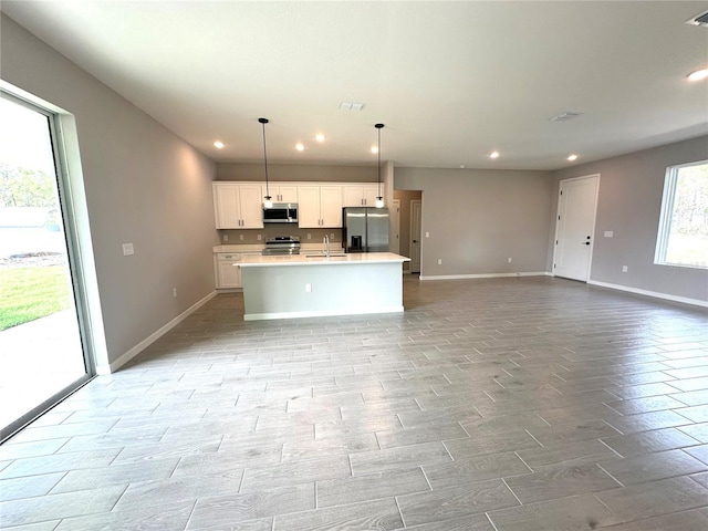 kitchen featuring appliances with stainless steel finishes, open floor plan, a kitchen island with sink, white cabinetry, and a sink