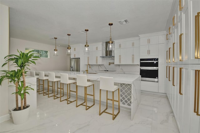 kitchen featuring hanging light fixtures, white cabinetry, stainless steel appliances, a spacious island, and a breakfast bar area