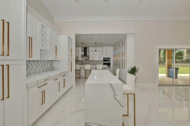 kitchen featuring white cabinets, backsplash, wall chimney exhaust hood, a kitchen island, and light stone countertops