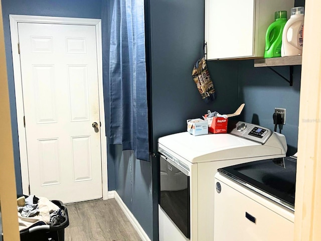 laundry room with washing machine and dryer, cabinets, and wood-type flooring