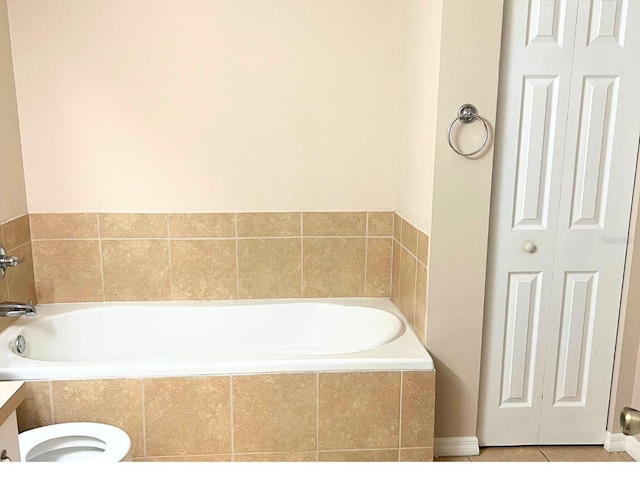 bathroom with tile patterned flooring, vanity, a relaxing tiled tub, and toilet