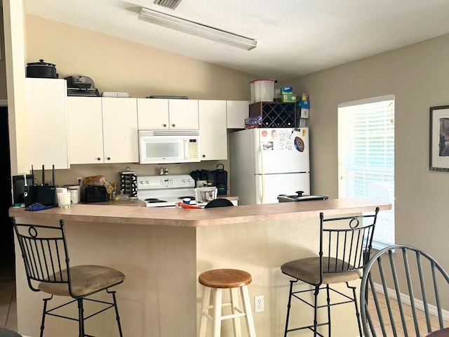 kitchen with white appliances, white cabinets, a kitchen breakfast bar, light tile patterned floors, and kitchen peninsula