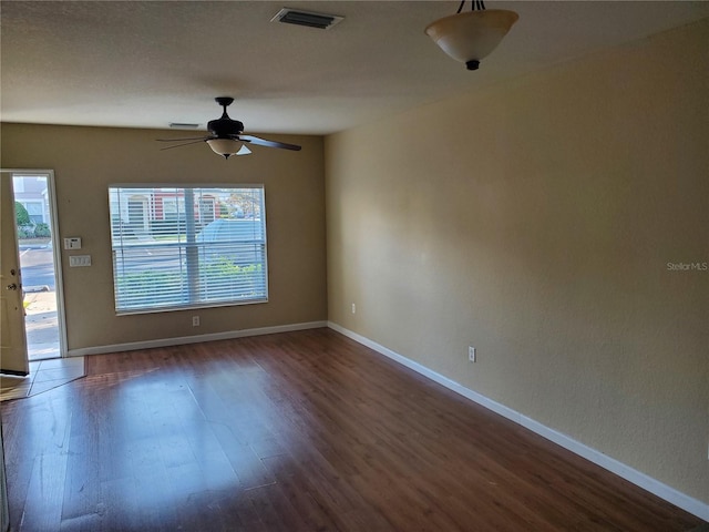 empty room featuring a wealth of natural light, dark wood-type flooring, ceiling fan, and a textured ceiling