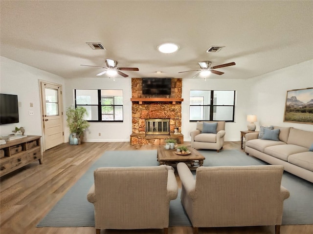 living room with wood-type flooring, ceiling fan, and a stone fireplace