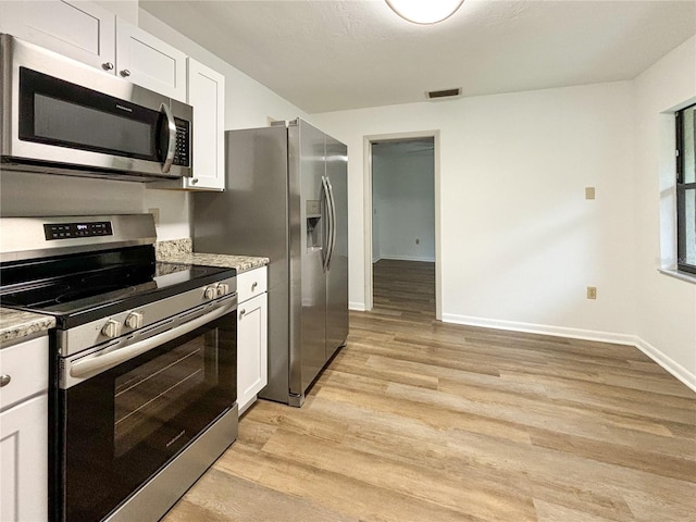 kitchen with stainless steel appliances, light stone counters, white cabinetry, and light hardwood / wood-style floors