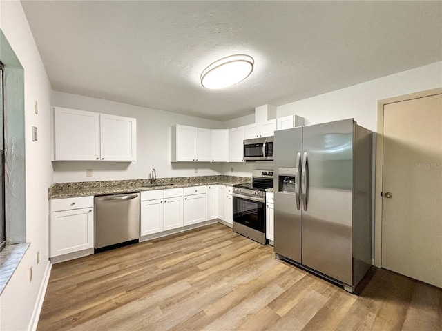 21389 SW 102nd Street Rd, Dunnellon, FL 34431 - kitchen featuring a sink, dark stone countertops, white cabinetry, light wood-style floors, and appliances with stainless steel finishes