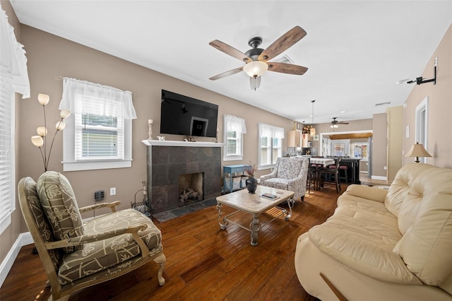 living room featuring ceiling fan, a tile fireplace, and dark wood-type flooring