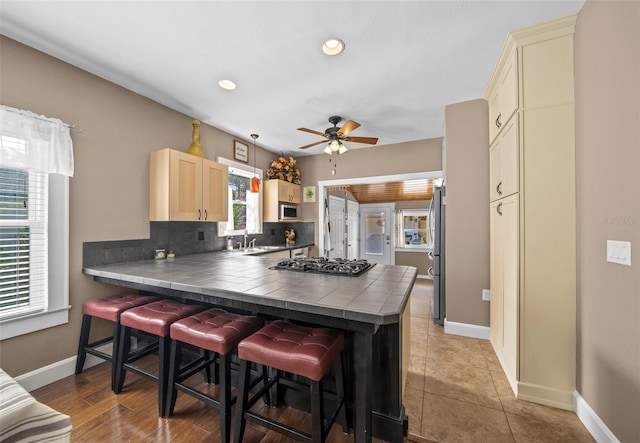 kitchen with a wealth of natural light, kitchen peninsula, tile counters, and a breakfast bar area