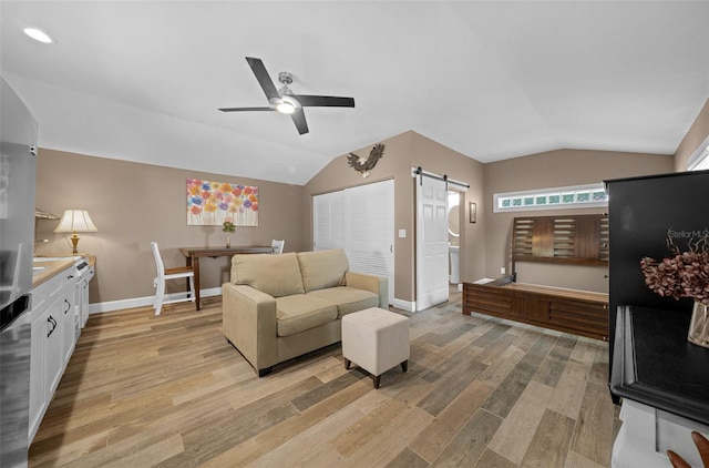 living room with a barn door, light hardwood / wood-style floors, vaulted ceiling, and ceiling fan