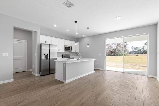 kitchen featuring white cabinetry, decorative light fixtures, light hardwood / wood-style flooring, appliances with stainless steel finishes, and an island with sink