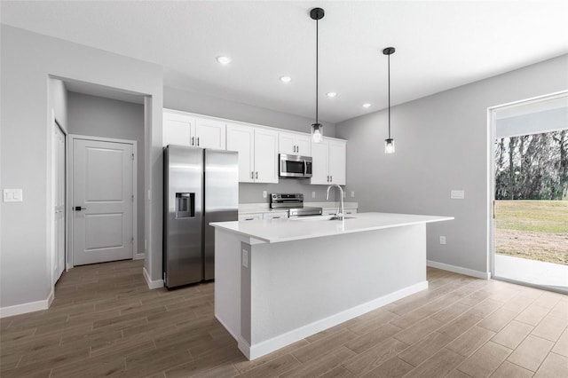 kitchen featuring decorative light fixtures, white cabinets, a kitchen island with sink, stainless steel appliances, and light wood-type flooring