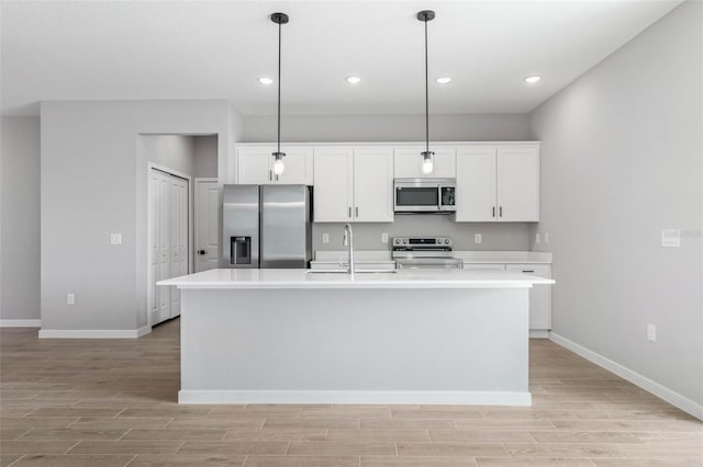 kitchen with pendant lighting, appliances with stainless steel finishes, sink, and an island with sink