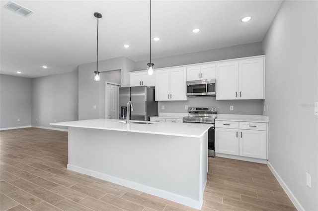 kitchen featuring sink, stainless steel appliances, white cabinets, a center island with sink, and decorative light fixtures