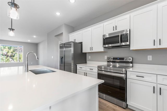 kitchen featuring appliances with stainless steel finishes, decorative light fixtures, sink, white cabinets, and light hardwood / wood-style flooring