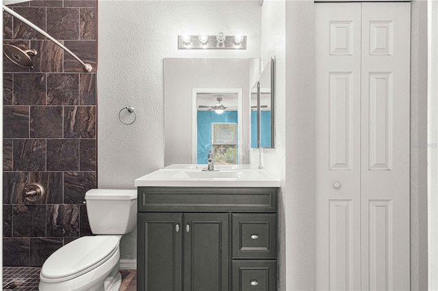 bathroom featuring ceiling fan, toilet, a tile shower, and vanity