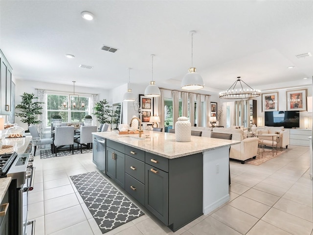 kitchen featuring hanging light fixtures, light stone countertops, appliances with stainless steel finishes, a notable chandelier, and a kitchen island with sink