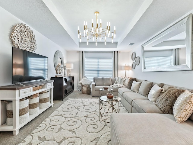 living room with a raised ceiling, a textured ceiling, a notable chandelier, and carpet flooring