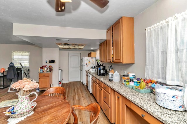 kitchen with white refrigerator, ceiling fan, light stone counters, stainless steel dishwasher, and light hardwood / wood-style flooring