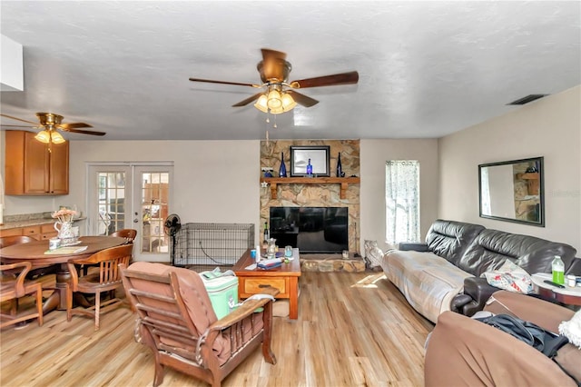 living room with light wood-type flooring, ceiling fan, french doors, and a stone fireplace