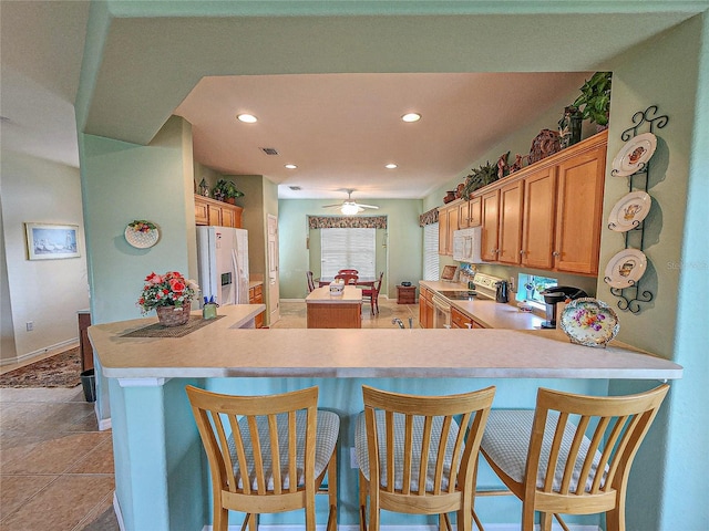 kitchen featuring a kitchen bar, white appliances, kitchen peninsula, and ceiling fan