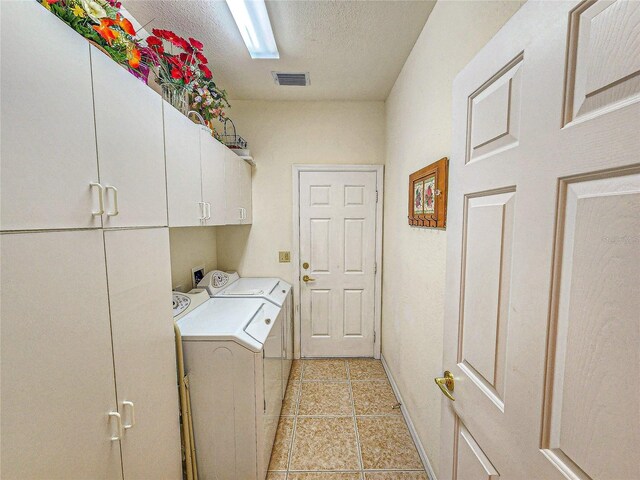 clothes washing area with washer and dryer, cabinets, light tile patterned flooring, and a textured ceiling