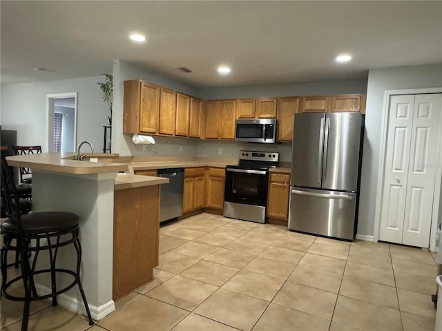 kitchen with appliances with stainless steel finishes, a kitchen breakfast bar, kitchen peninsula, and light tile patterned flooring