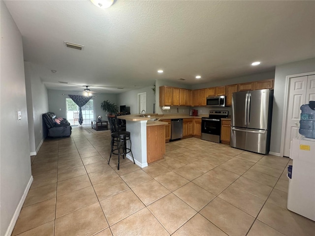 kitchen with stainless steel appliances, a kitchen breakfast bar, kitchen peninsula, sink, and ceiling fan