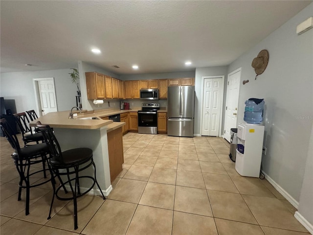 kitchen with a breakfast bar area, light tile patterned floors, stainless steel appliances, sink, and kitchen peninsula