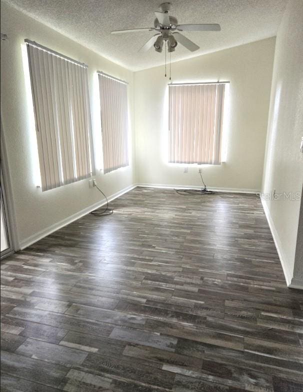 empty room with dark wood-style floors, ceiling fan, baseboards, and a textured ceiling