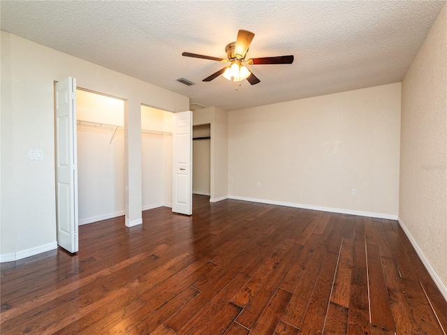 unfurnished bedroom featuring multiple closets, a textured ceiling, ceiling fan, and dark wood-type flooring