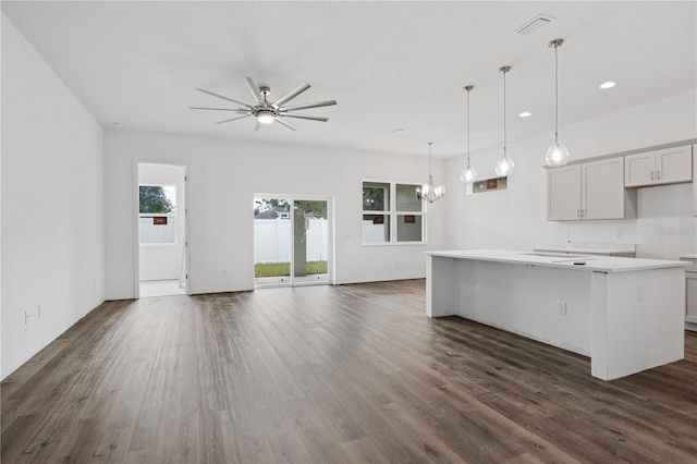 kitchen with a kitchen island with sink, ceiling fan with notable chandelier, a kitchen bar, hanging light fixtures, and dark hardwood / wood-style floors