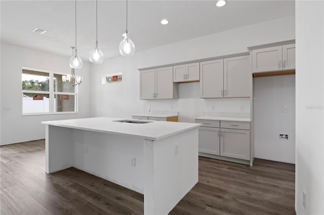 kitchen with a center island with sink, decorative light fixtures, gray cabinets, and dark hardwood / wood-style flooring