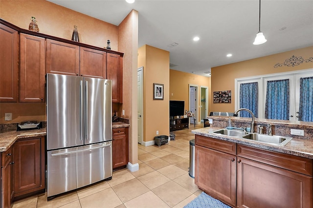 kitchen with hanging light fixtures, light stone counters, stainless steel refrigerator, and sink