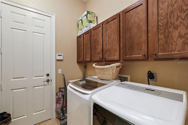 clothes washing area featuring light tile patterned floors, cabinets, and washing machine and dryer