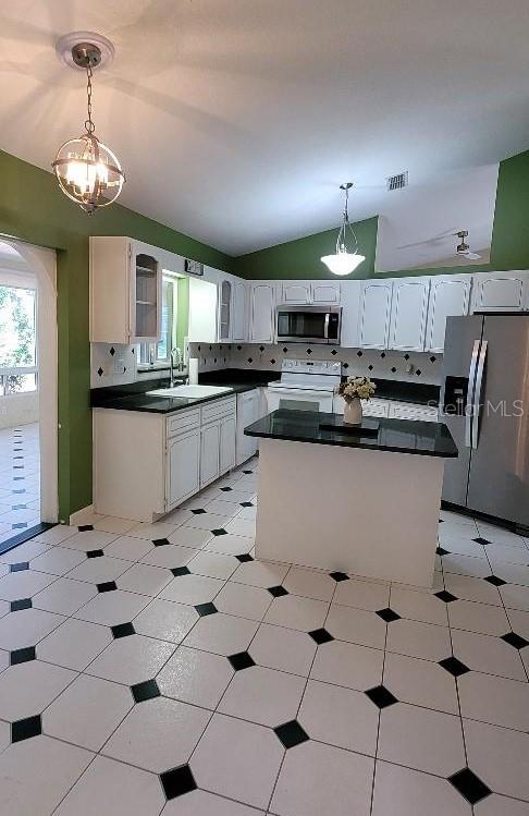 kitchen with a center island, stainless steel appliances, backsplash, lofted ceiling, and white cabinets