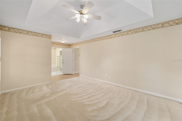 carpeted spare room featuring a tray ceiling and ceiling fan