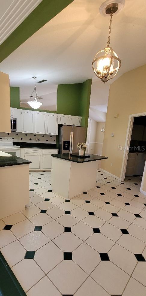 kitchen with white cabinetry, a center island, stainless steel appliances, an inviting chandelier, and pendant lighting