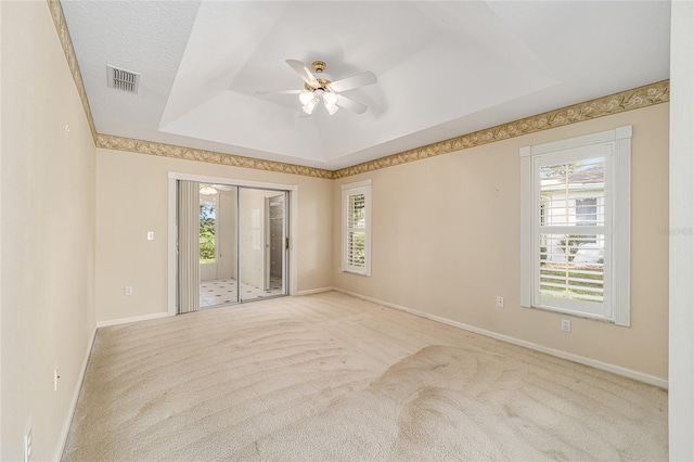 carpeted spare room featuring ceiling fan, a raised ceiling, and a wealth of natural light