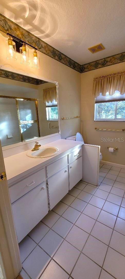 bathroom with vanity, a textured ceiling, a shower with shower door, and tile patterned flooring