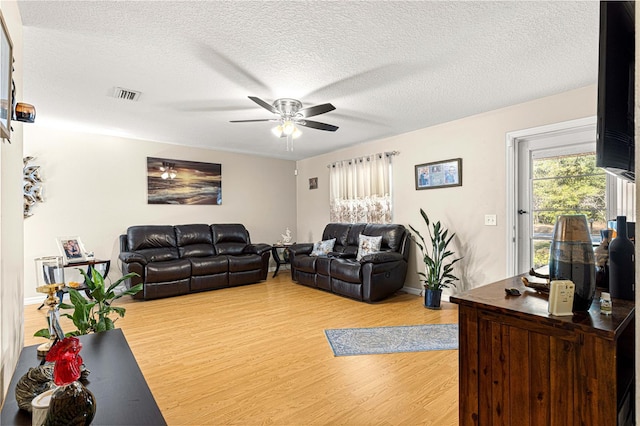 living room with ceiling fan, a textured ceiling, and light wood-type flooring