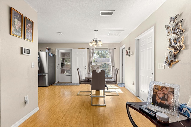 dining space featuring a textured ceiling, a chandelier, and light hardwood / wood-style floors