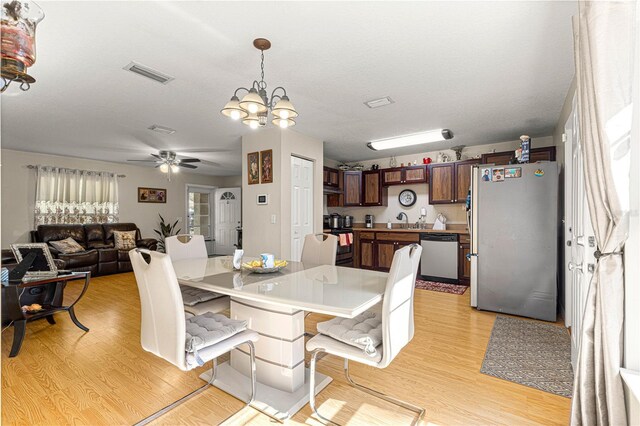 dining room with sink, ceiling fan with notable chandelier, a textured ceiling, and light wood-type flooring