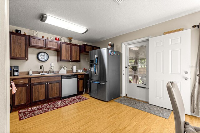 kitchen featuring sink, stainless steel appliances, dark brown cabinetry, a textured ceiling, and light wood-type flooring