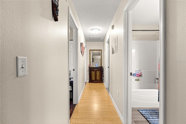 corridor featuring a textured ceiling and light wood-type flooring