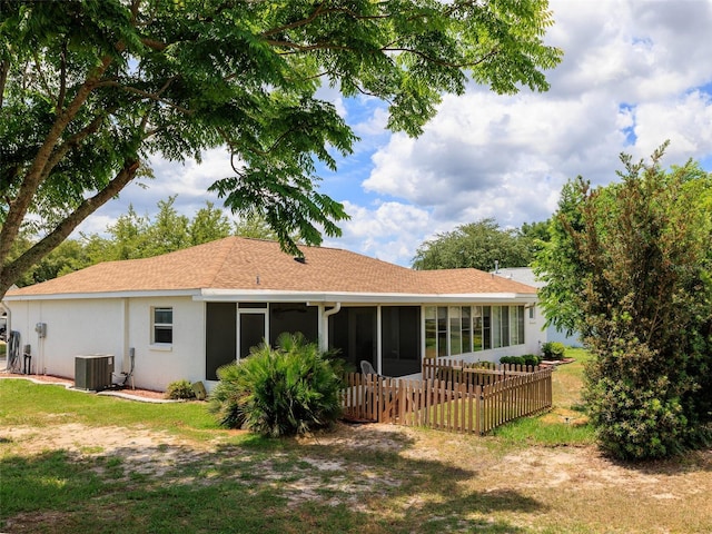 rear view of property with central AC unit, a sunroom, and a lawn