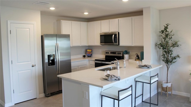 kitchen with a breakfast bar area, kitchen peninsula, white cabinets, and appliances with stainless steel finishes