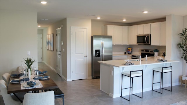 kitchen with white cabinetry, kitchen peninsula, a kitchen bar, light tile patterned flooring, and appliances with stainless steel finishes