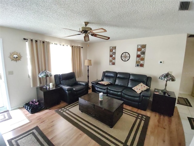 living room featuring ceiling fan, visible vents, a textured ceiling, and wood finished floors